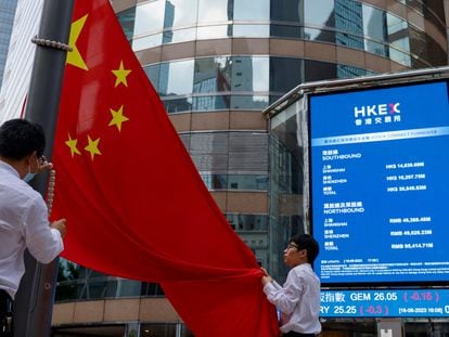 Dos personas despliegan una bandera de China frente a un monitor donde se recoge la evolución de la Bolsa de Hong Kong.