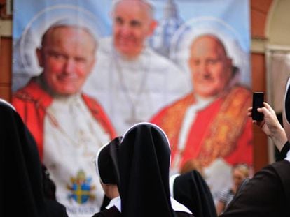 Varias monjas observan y fotografían un panel con la imagen de varios pontífices. 
 