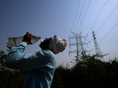 Un trabajador bebe agua junto a unos tendidos eléctricos durante la ola de calor en Nueva Delhi, India.