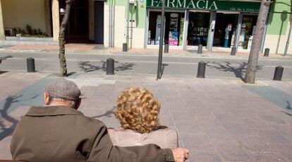Una pareja de pensionistas ante una farmacia.