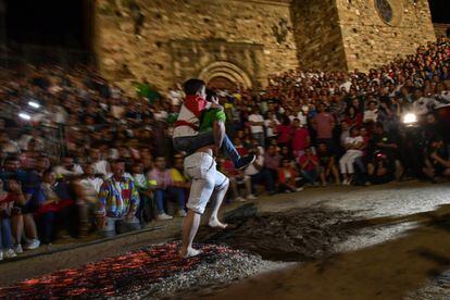 Un hombre lleva a un niño a su espalda mientras camina sobre las brasas durante la noche de San Juan en San Pedro Manrique (Soria).