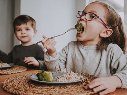 Siblings eat a healthy vegan lunch of broccoli and brown rice at home.