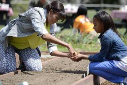 La primera dama estadounidense, Michelle Obama (i) ayuda a Ariana Docanto (d), una estudiante de quinto curso en la escuela de  Arthur D. Healey, a plantar semillas durante la quinta edición de cultivo de la Casa Blanca celebrada en el jardín sur de la residencia presidencial en Washington, Estados Unidos.