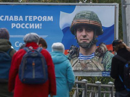 Varias personas en una parada de tranvía, frente a un cartel que mostraba este miércoles a un soldado ruso con la leyenda “Gloria a los héroes de Rusia”, en San Petersburgo.