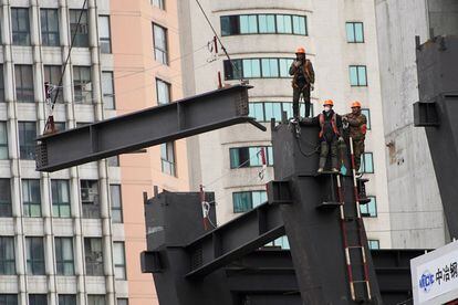 Unos trabajadores contemplan cómo una grúa eleva una estructura en una obra en Shanghái el viernes pasado