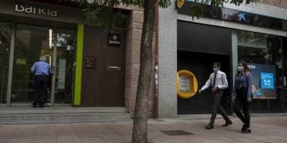 Varias personas caminan al lado de una oficina de Bankia y otra de CaixaBank.