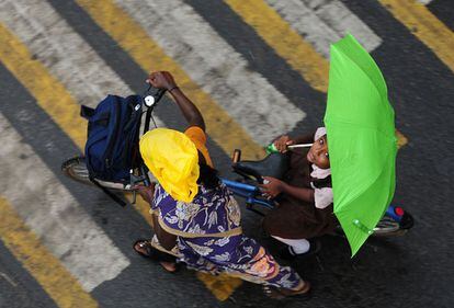 Una niña india sostiene un paraguas mientras se sienta en una bicicleta al cruzar una carretera durante las lluvias fuertes en Chennai.