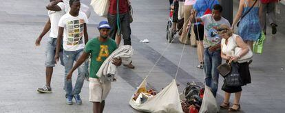 Los manteros recogen su mercancía ante la mirada de una posible cliente en la calle Preciados.