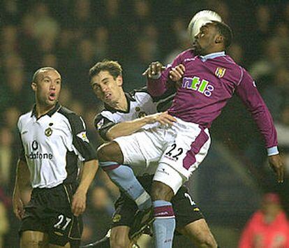 Vasell, del Aston Villa, le gana la pelota al defensa del Manchester Gary Neville.