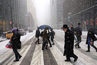 Varios peatones cruzan una calle bajo la nieve en Nueva York.