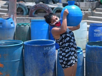 Una residente del barrio Los Almendros, en Ciudad Delgado (El Salvador) acarrea un recipiente con agua recibida de la Cruz Roja.