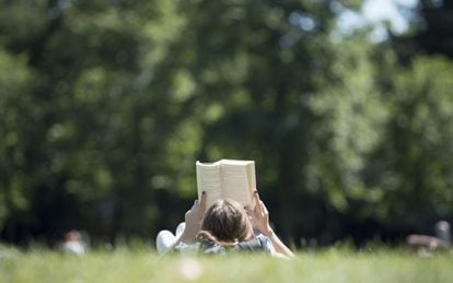 Una mujer descansa en el césped leyendo un libro un caluroso día de verano en el jardín del Palacio de Osnabrück, Alemania.