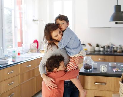 Una madre abraza con fuerza a sus hijos en la cocina.