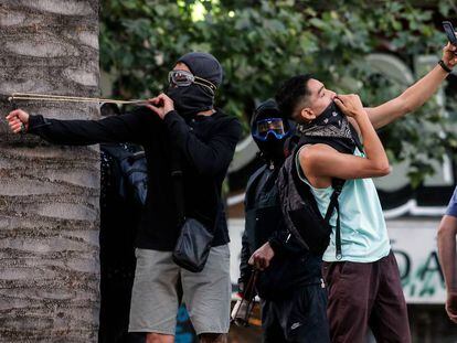 Un joven se hace un selfi mientras otro apunta un tirachinas durante una protesta en Santiago de Chile.