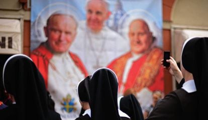 Varias monjas observan y fotografían un panel con la imagen de varios pontífices. 
 