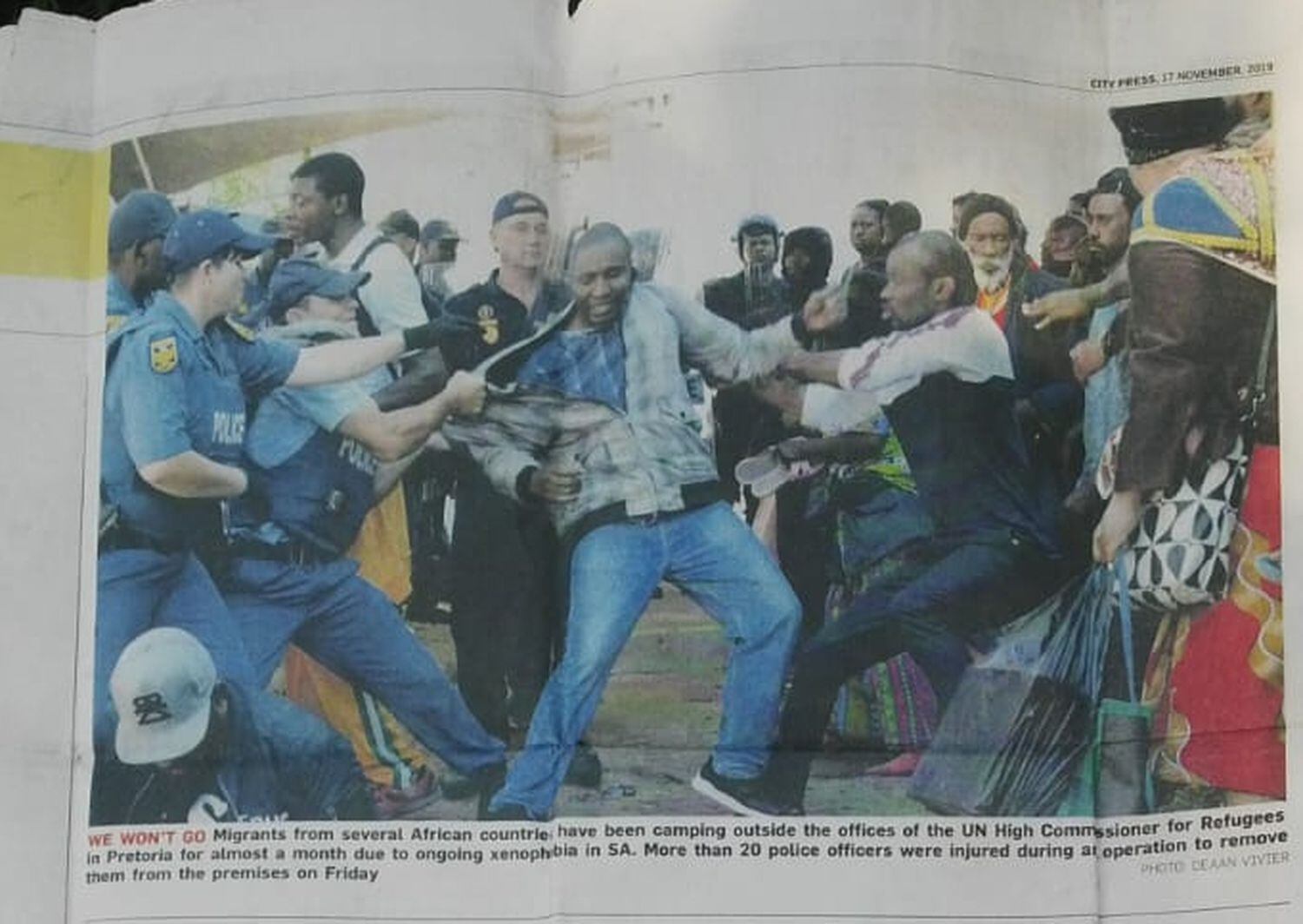 Imagen de un recorte de periódico local que recoge la noticia sobre el desalojo de cientos de solicitantes de asilo en la sede de la UNCHR en Pretoria (Sudáfrica) y su posterior detención, en noviembre de 2019. En la fotografía del periódico se distingue a John Nkobo y a Jerry Lumbela.