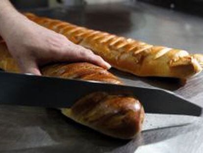 Un repostero corta una barra de pan en una pastelería de España.