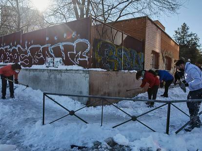 Varios familiares colaboran en la limpieza del hielo y la nieve en las inmediaciones del colegio Amadeo Vives tras la gran nevada por el paso de la borrasca 'Filomena', en Madrid.