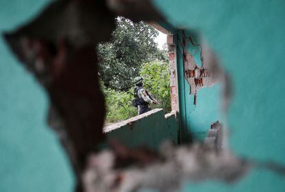 Un soldado visto a través de un hoyo en uno de los muros de una vivienda afectada en la comunidad de Ojo de Agua.