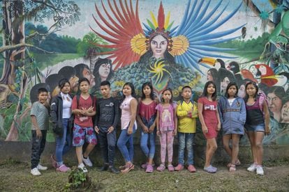 Alumnos y alumnas indígenas del internado Indígena de San Francisco de Loretoyaco, en Puerto Nariño (Colombia) delante de un mural que relata la historia de los clanes de la cultura ticuna en una de las paredes de la escuela.