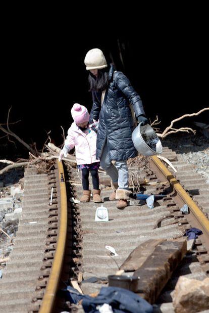 Una mujer atraviesa con su hija un tramo de vía de ferrocarril destrozado por el tsunami.