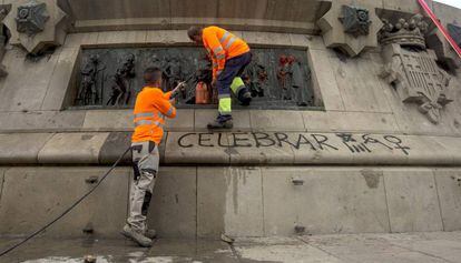 Dos operarios limpian las pintadas en el monumento a Col&oacute;n.