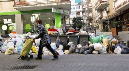 Una mujer pasa ante un grupo de contenedores rodeados de bolsas de basura, en una calle de Alcorc&oacute;n.
