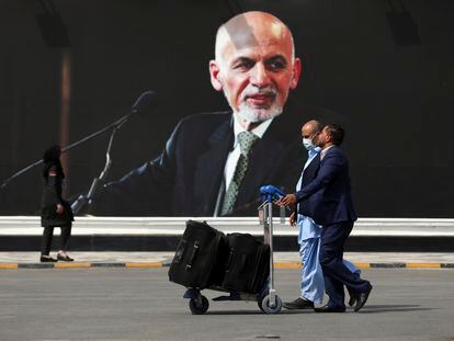 Pasajeros en el aeropuerto de Kabul pasan junto a la imagen del por entonces presidente de Afganistán, Ashraf Ghani, el 14 de agosto, con los talibanes ya cercando la capital.