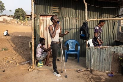 Lahai Makieu (centro) se cepilla la barba mientras su prometida, Zainab Turay (derecha) encuentra un asiento frente a su casa en la comunidad de Yams Farm, en Freetown, el 15 de abril de 2022. Makieu, de 49 años, es el entrenador del equipo de fútbol. Los rebeldes le dispararon en 1992. Cuando llegó al hospital había perdido tanta sangre y su pierna estaba en tan mal estado que los médicos se la tuvieron que cortar.