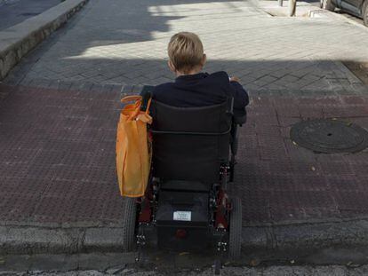 Una mujer en silla de ruedas sube un bordillo en una calle de Madrid. 