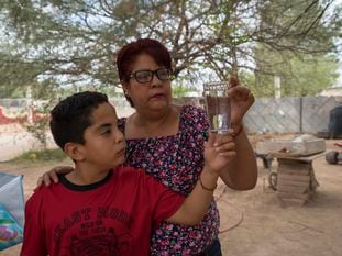 Marisol y su hijo, habitantes de Bacanuchi, observan un vaso de agua corriente, que no pueden beber desde el derrame de 2014.