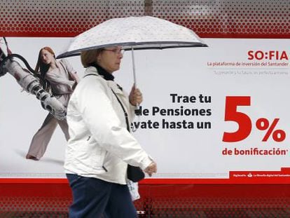 Una mujer camina frente a una sucursal bancaria en la que se anuncian planes de pensiones.