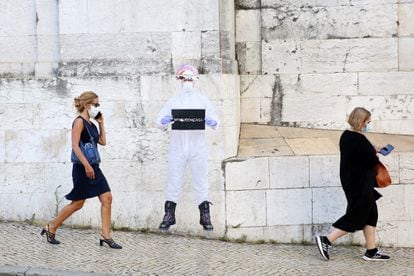 Mujeres con mascarilla pasean por Lisboa ante un cartel que dice "quédense en casa"