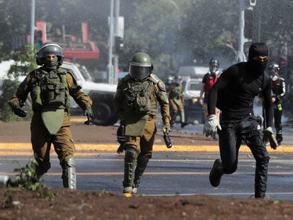 Un manifestante huye de dos policías durante una manifestación por el tercer aniversario del estallido social, este martes en Santiago de Chile.