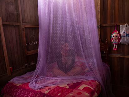 Valentina Esperanza, que se está recuperando del dengue, sentada en su cama protegida con mosquitera mientras ve un programa de televisión en su casa de Pucallpa, en la región Ucayali de Perú.