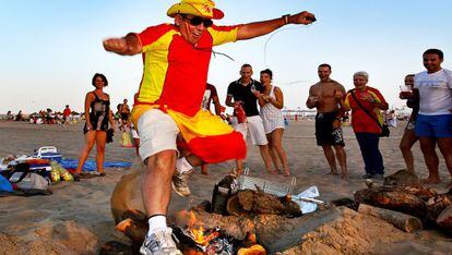 Un hombre ataviado con la bandera de Espa&ntilde;a salta una de las primeras hogueras encendidas en la playa en Valencia. 