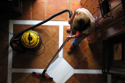 Una empleada del hogar limpia el suelo con un aspirador.