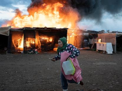 Una mujer corre junto a chabolas en llamas durante un incendio antes del desalojo en el asentamiento El Walili, en Níjar (Almería), este lunes.