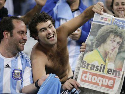 Dos aficionados argentinos se recrean con la eliminaci&oacute;n de Brasil mostrando un peri&oacute;dico local en las gradas del Arena Corinthians de S&atilde;o Paulo
