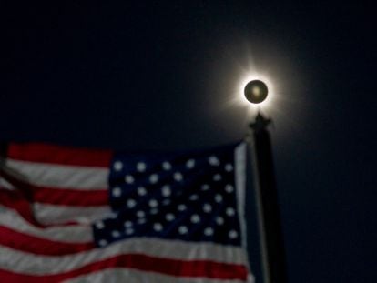 Un eclipse solar total se ve junto a una bandera estadounidense ondeando en Houlton, Maine, EE.UU. 8 de abril de 2024.