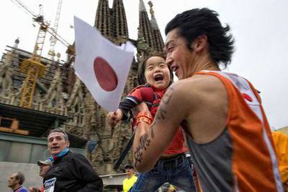 Un ciudadano japonés, que participó en la maratón, alza a su hija en brazos a su paso por la Sagrada Familia. La carrera fue seguida por innumerables personas durante todo su recorrido por las calles de Barcelona.