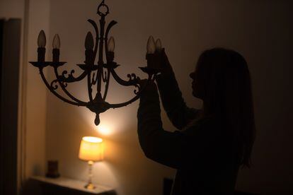 Una joven desenrosca una bombilla de una lampara para reducir el consumo en su vivienda.