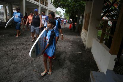 Uno de los beneficiarios del programa Surfitsmo carga una tabla de surf mientras se dirige a una de las playas de Chiltiupán.