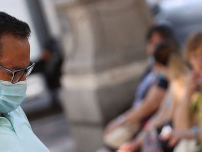 Un ciudadano con mascarilla revisa su teléfono en una calle del centro de Madrid