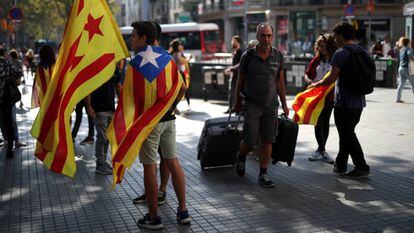 Un turista camina cerca de Plaza Catalunya, en Barcelona, junto a un grupo de jóvenes con banderas.