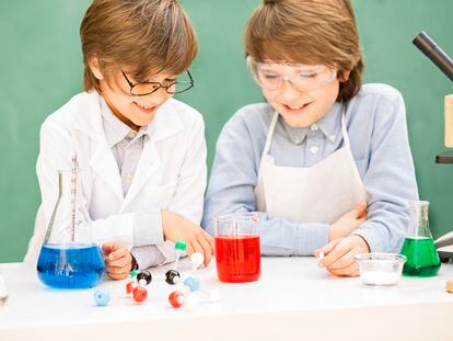 Two elementary-age children collaborate on various science experiments.  They are using a microscope, scale, chemical glassware, chemicals.  Imagination, creativity, inspiration for these little chemists!  DNA molecule.  Chalkboard, classroom setting.