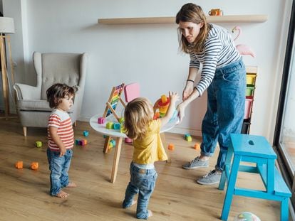 Positive young female babysitter in casual clothes playing with infant children in cozy playroom with colorful educational toys. Child education concept learn to share