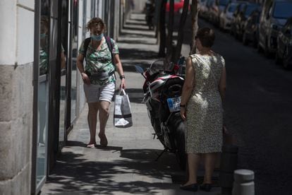 Dos mujeres intentan caminar por una acera estrecha donde está estacionada una motocicleta, este jueves en Madrid. 
