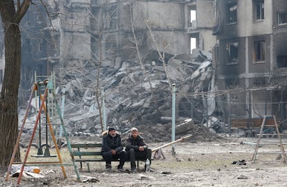 Two neighbors sit on a bench in front of buildings destroyed by shelling in Mariupol on March 25.