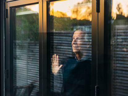 Un hombre mayor mira el atardecer por su ventana.